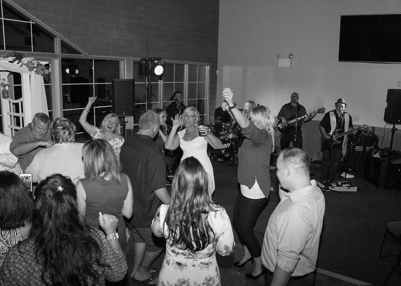 People dancing and celebrating at an indoor party with a live band performing in the background.